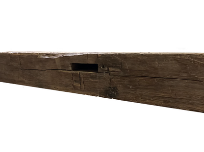 close up of a natural colored hand hewn beam showing a mortise pocket prominently displayed. Mortise pockets are a rectangular opening in the beam. Light axe marks displayed as well.
