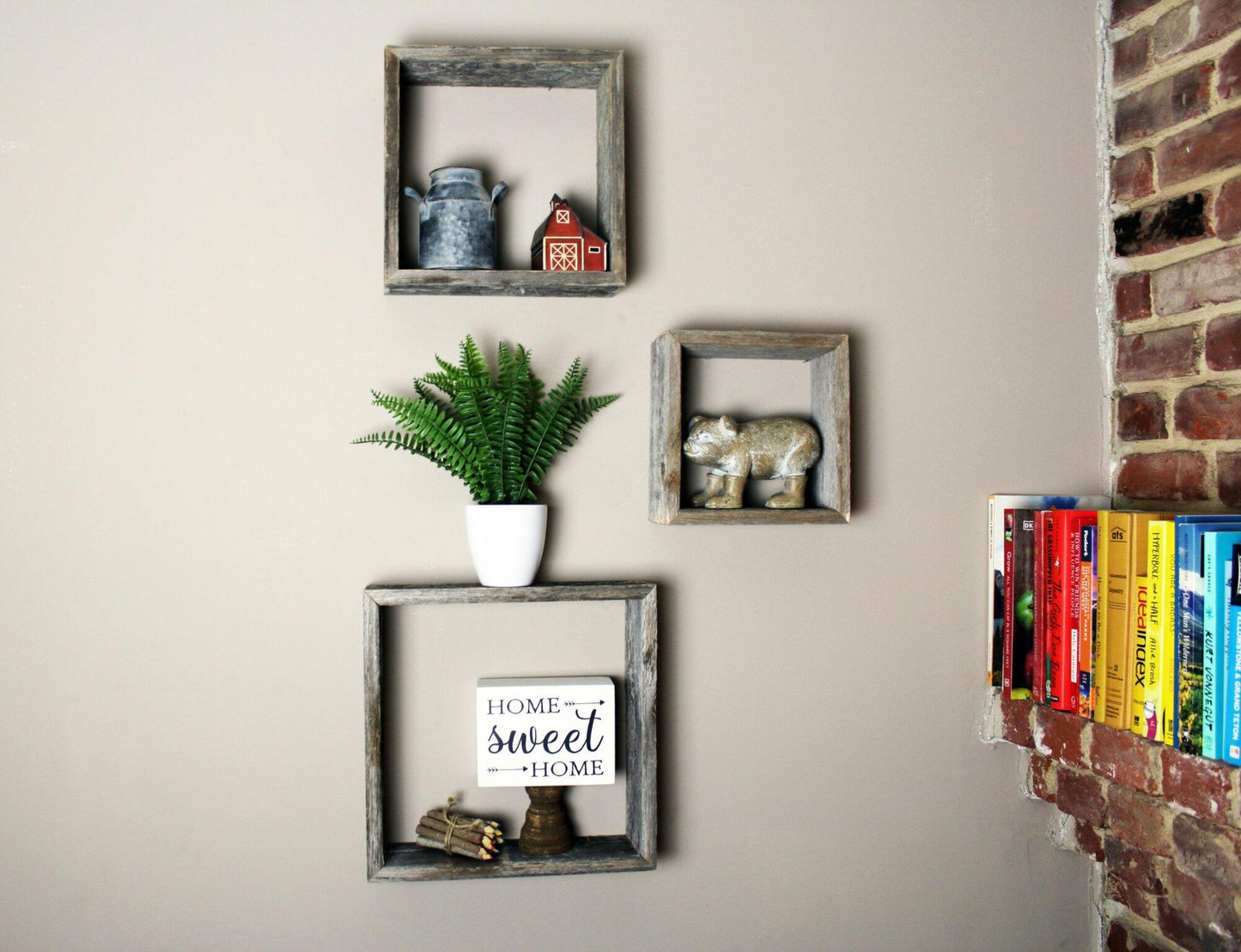 three open box floating shelves in small, medium, and large sizes. Open box shelves shown decorated on a wall next to a brick wall with books displayed.