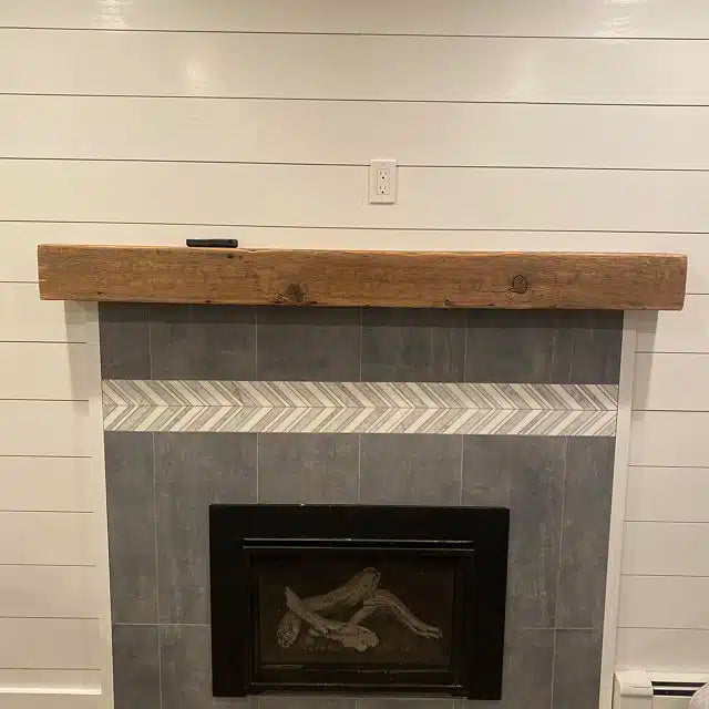 a reclaimed wood rustic fireplace mantel. The mantel is the natural color of the wood with knots present. It is mounted over a tile fireplace on a shiplap wall.