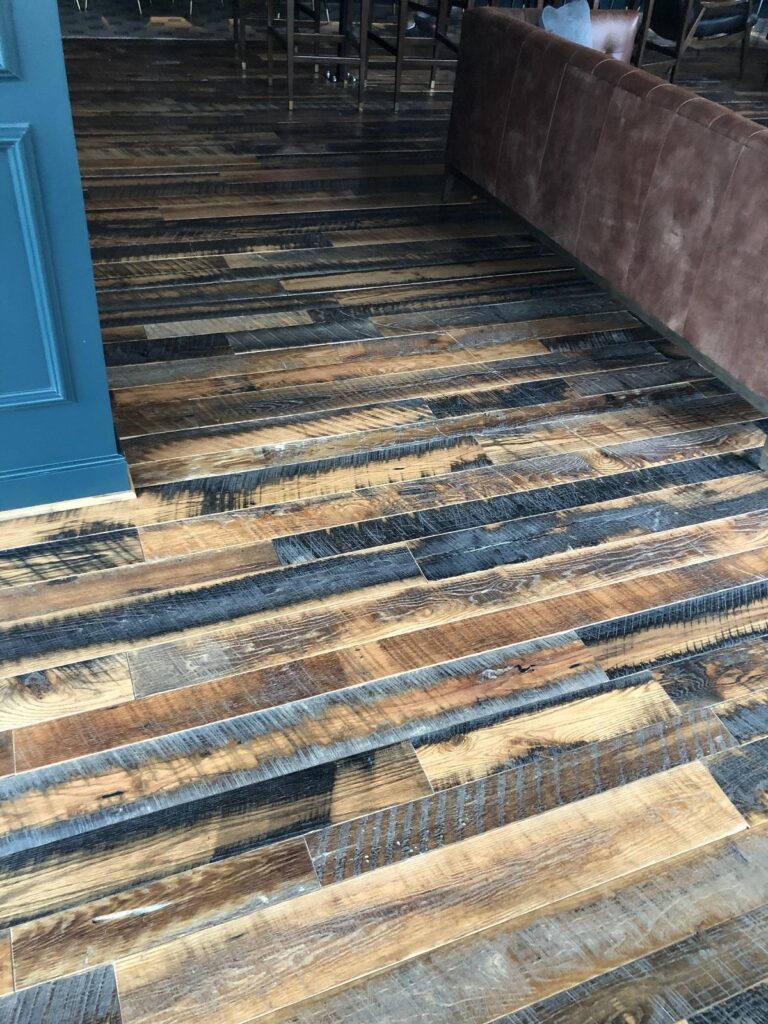 close up of Heartland Barnwood Oak Red & White Mixed Skip-Planed Brown wood flooring  with brown couch and blue wall