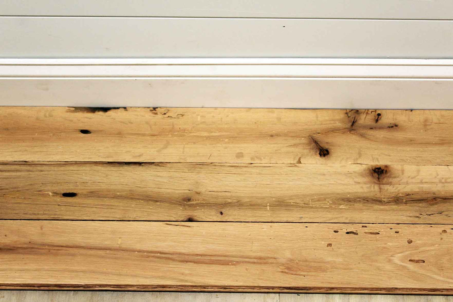 red oak reclaimed flooring installed with baseboard molding. Variations in wood color and grain pattern, knots, and characteristics from previous bug activity shown.