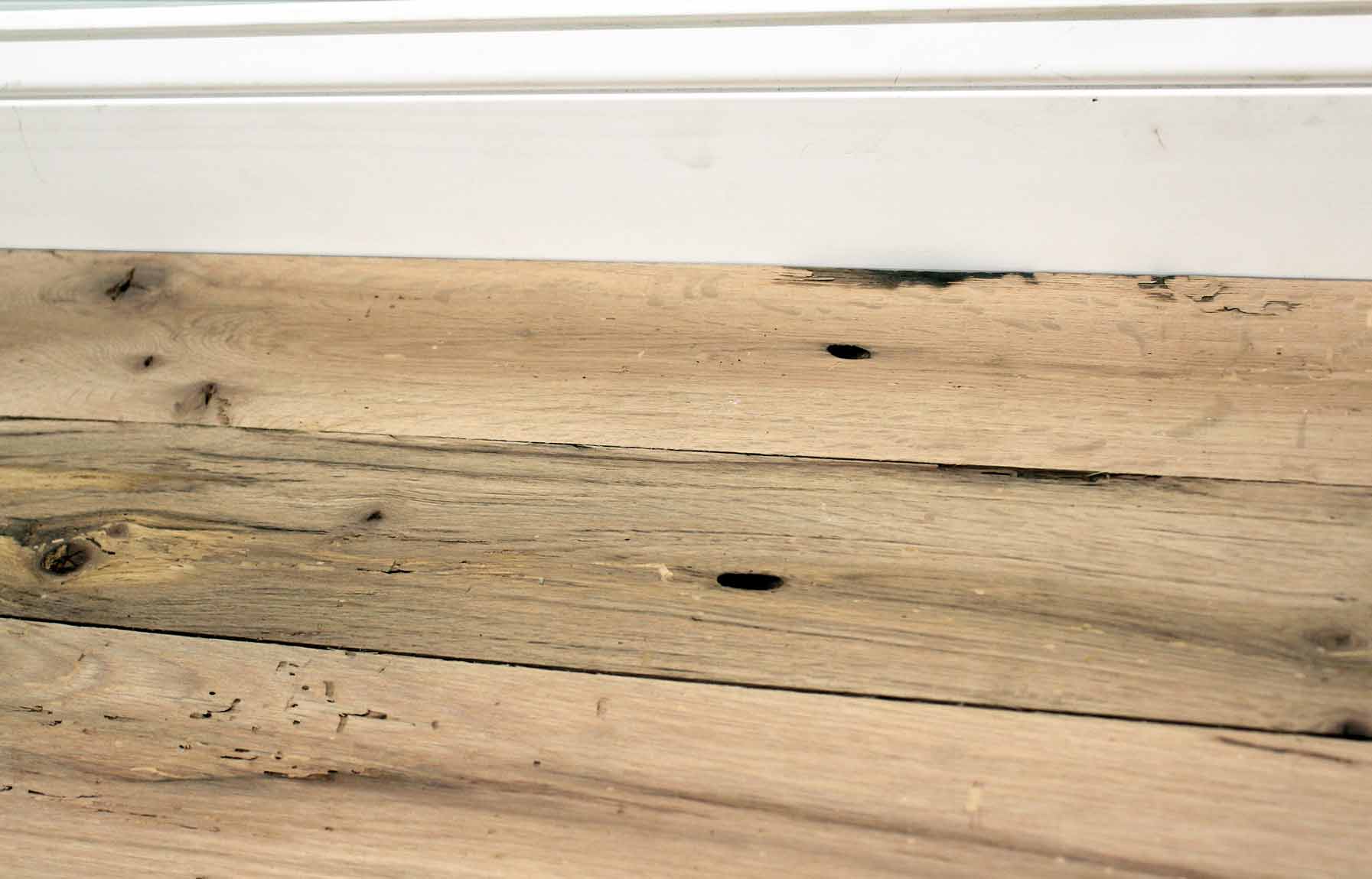 red oak reclaimed flooring installed with baseboard molding. Variations in wood color and grain pattern, knots, and characteristics from previous bug activity shown.