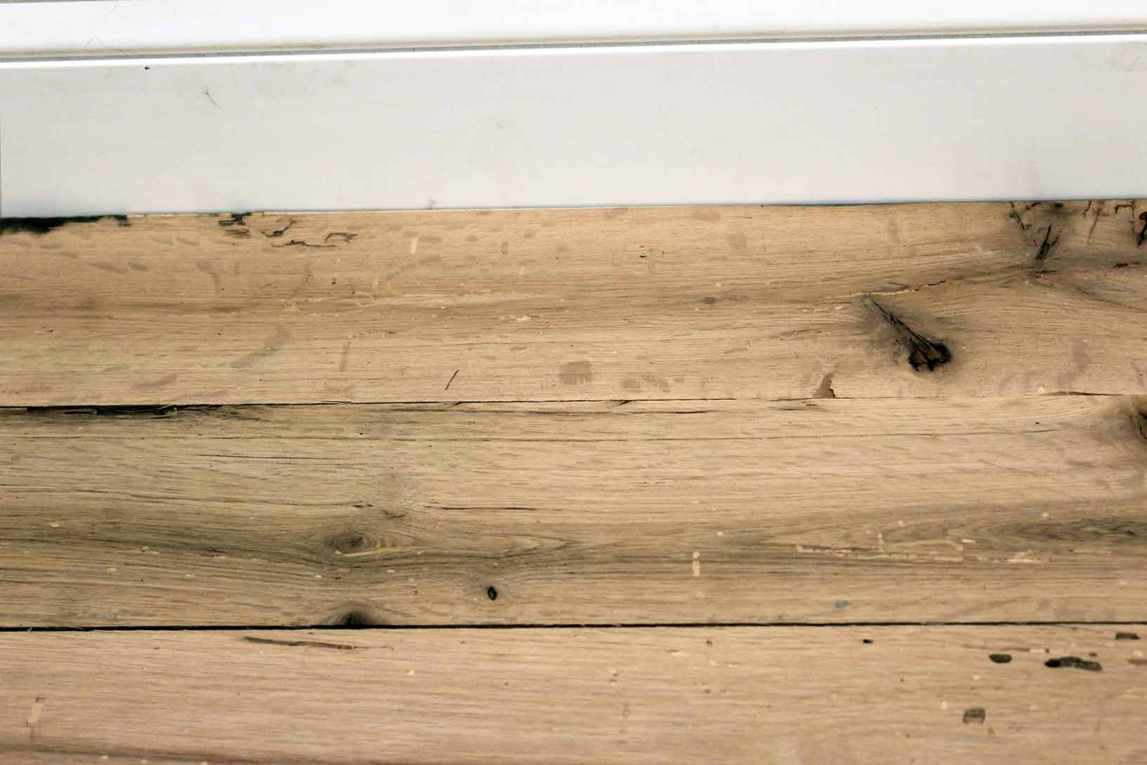 red oak reclaimed flooring installed with baseboard molding. Variations in wood color and grain pattern, knots, and characteristics from previous bug activity shown.