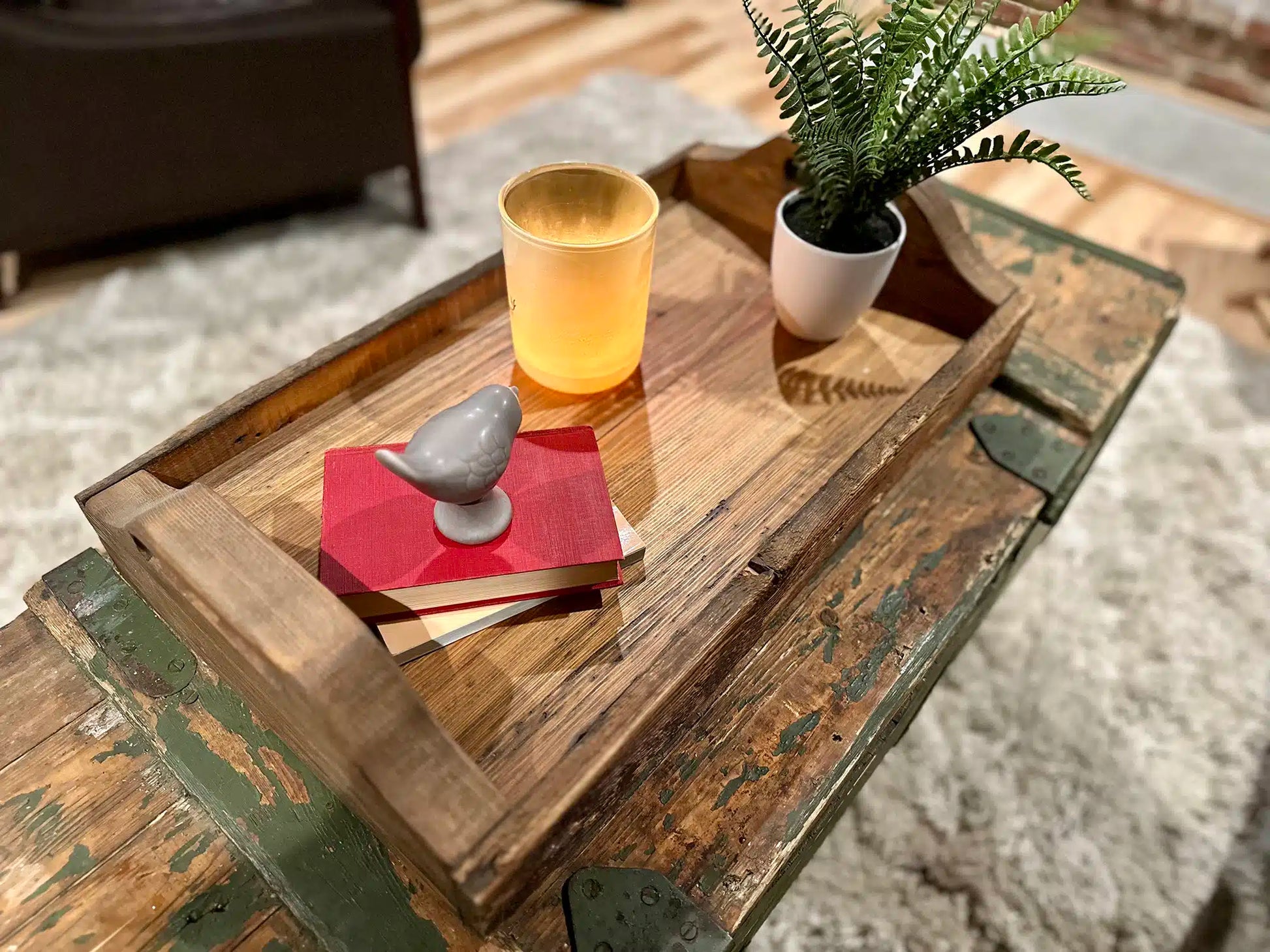 wood serving tray in a top down view displayed on an old army chest. Shows rounded handles, characteristics in the wood, and decor items placed on top.