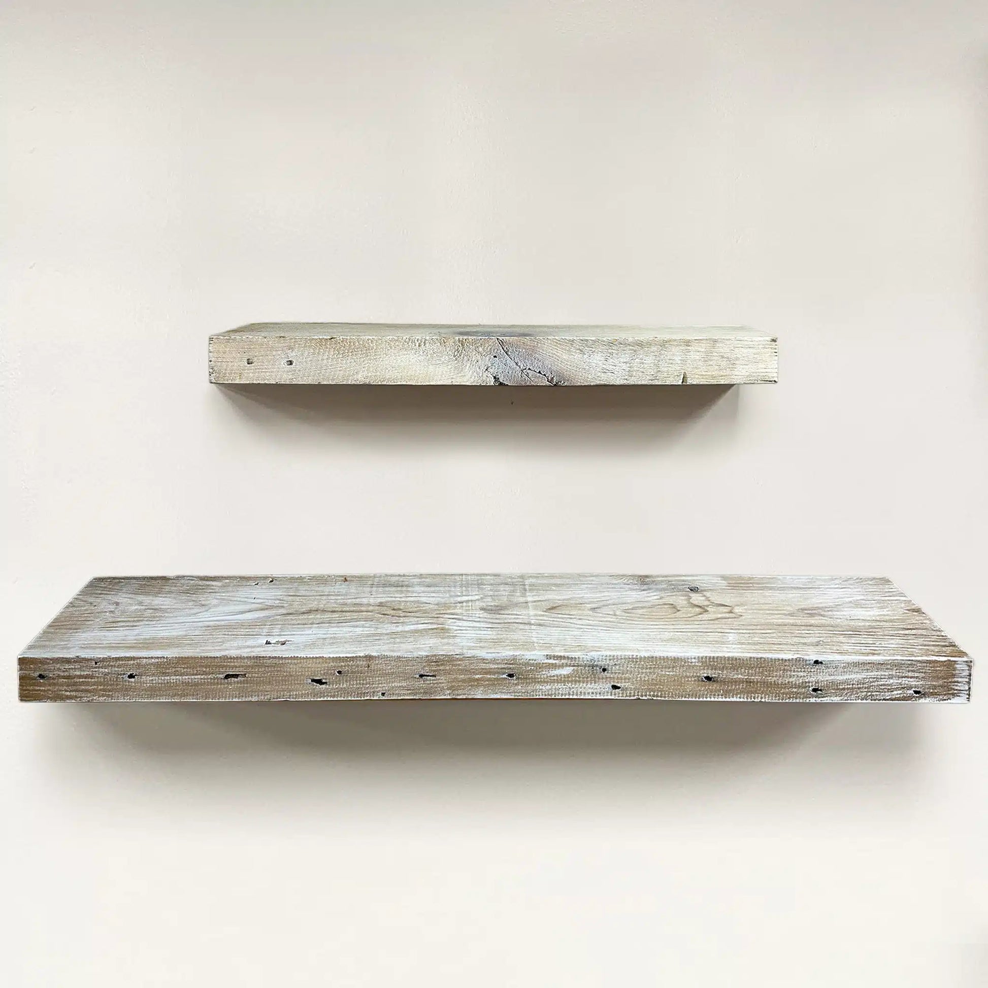 a set of two reclaimed wood floating shelves in the white wash finish. White wash application, knots, grain patterns, and nail holes are shown in the wood.