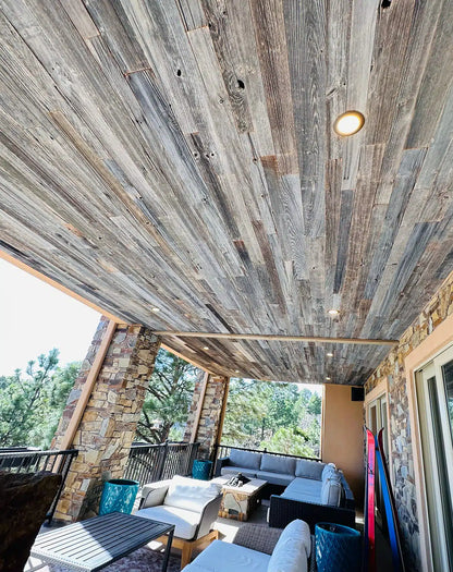 weathered grey barnwood paneling installed on a ceiling of an outdoor sunroom. Variations of color, texture, and characteristics displayed throughout. 