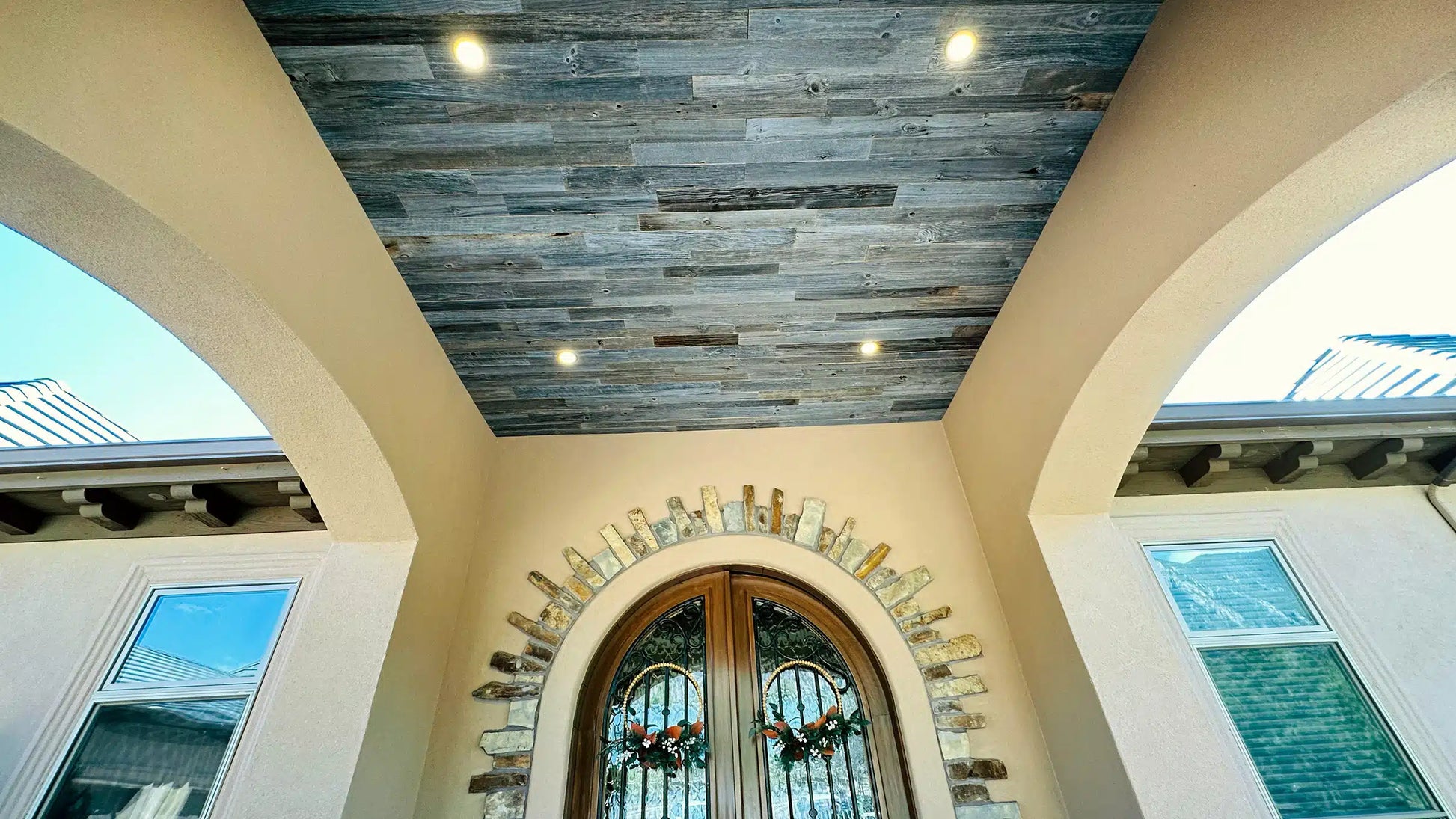 weathered grey barnwood paneling installed on a ceiling of an outdoor sunroom. Variations of color, texture, and characteristics displayed throughout.