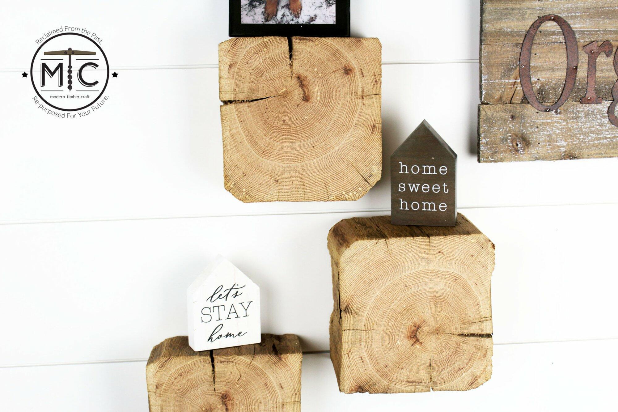 a set of three reclaimed wood wall blocks. The front facing sides are a fresh cut end displaying the growth rings and checking in the wood. The three blocks are staggered on the wall with minimal decor.