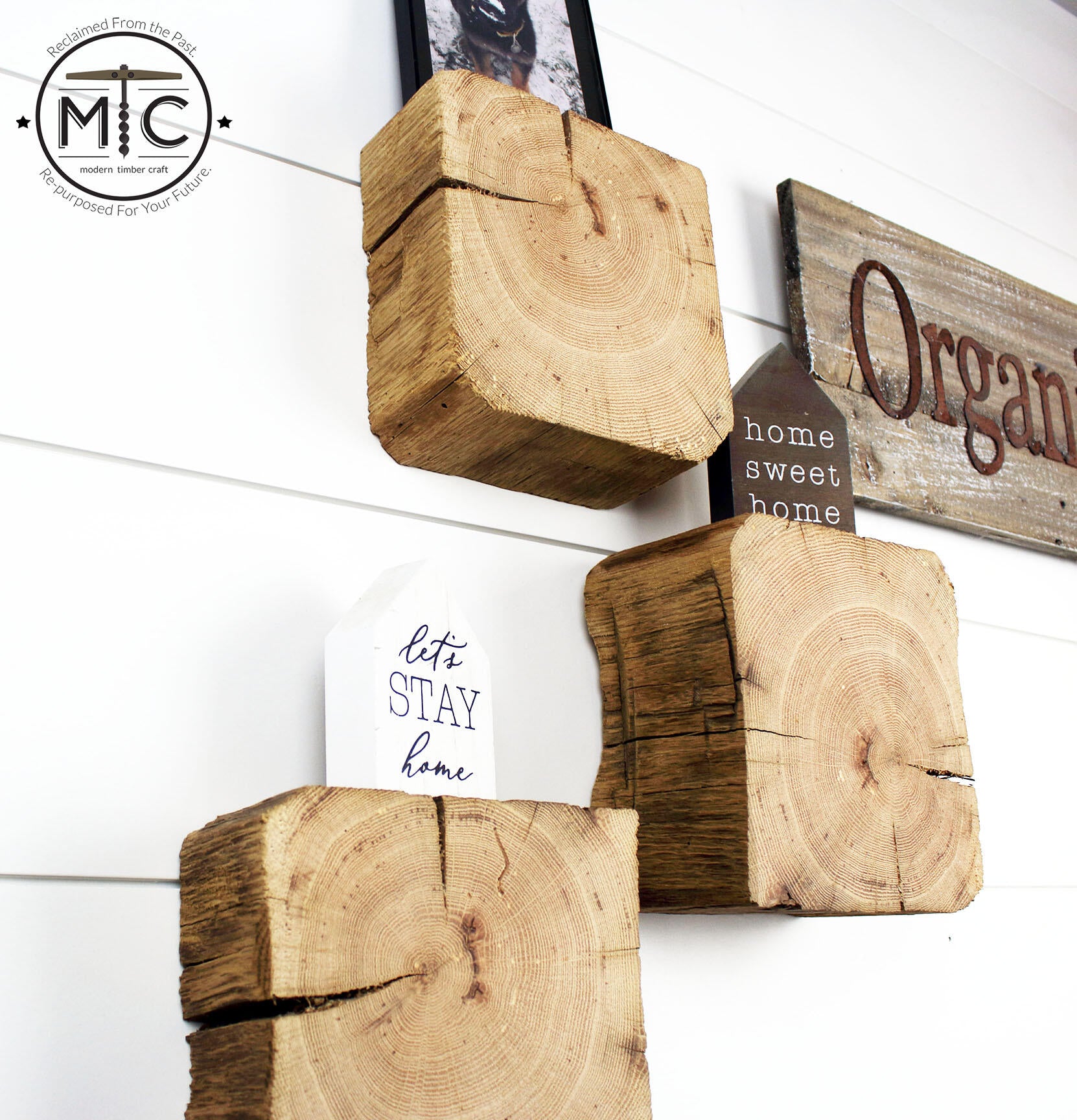 a set of three reclaimed wood wall blocks. The front facing sides are a fresh cut end displaying the growth rings and checking in the wood. The three blocks are staggered on the wall with minimal decor. This angle shows the aged layer of material and characteristics in the blocks.