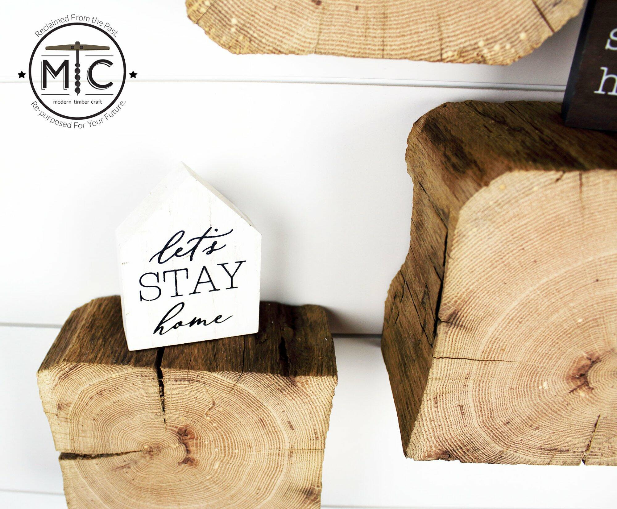 a close up of a set of three reclaimed wood wall blocks. The front facing sides are a fresh cut end displaying the growth rings and checking in the wood. The three blocks are staggered on the wall with minimal decor. This angle shows the aged layer of material and characteristics in the blocks.
