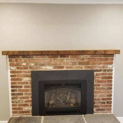 a reclaimed wood floating fireplace mantel mounted above a traditional brick fireplace. Nail holes and color variations are prominently displayed in the face of the mantel.
