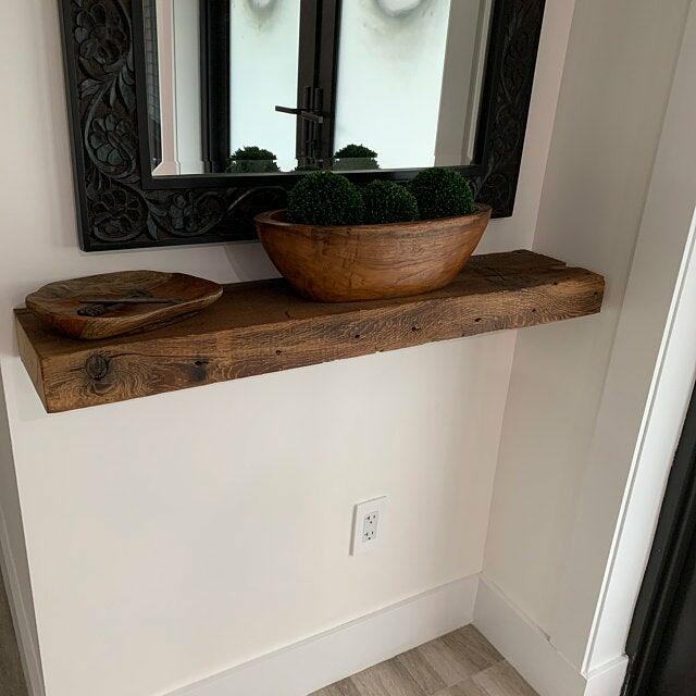a reclaimed barnwood floating shelf mounted in an entryway. Knots and grain patterns are highlighted on the front of the piece.