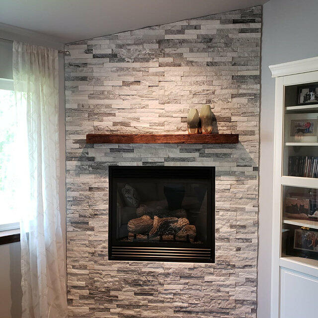 reclaimed barnwood fireplace mantel displayed on a stone fireplace. Minimal decor on mantel with a light shining down to perfectly highlight the mantel.