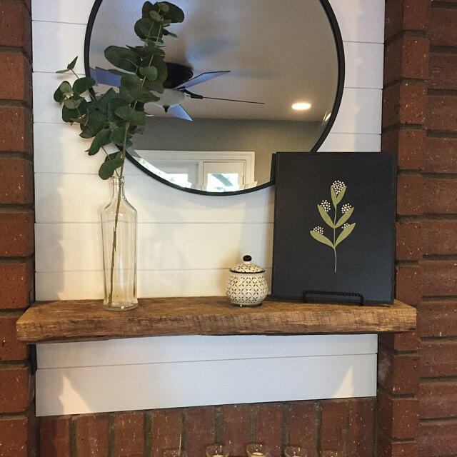 a reclaimed barnwood floating shelf shown surrounded by brick. The mantel is rounded on the front edges with saw marks prominent.