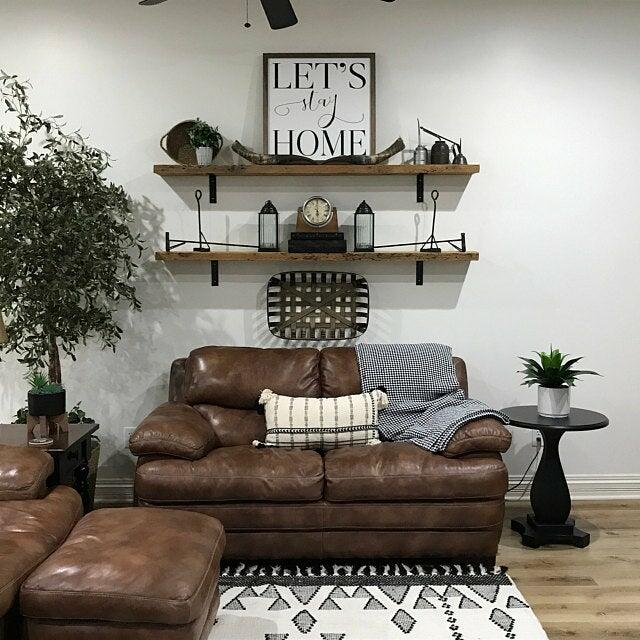 two reclaimed barnwood wall shelves shown in a living room over a loveseat. Shelves are shown in the natural option and decorate with vintage items to give a farmhouse feel.