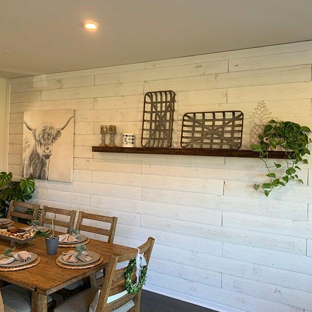 reclaimed barnwood floating shelf mounted on a light, wood wall in a dining room. Surround by rustic decor and plants, the mantel is the focal point.