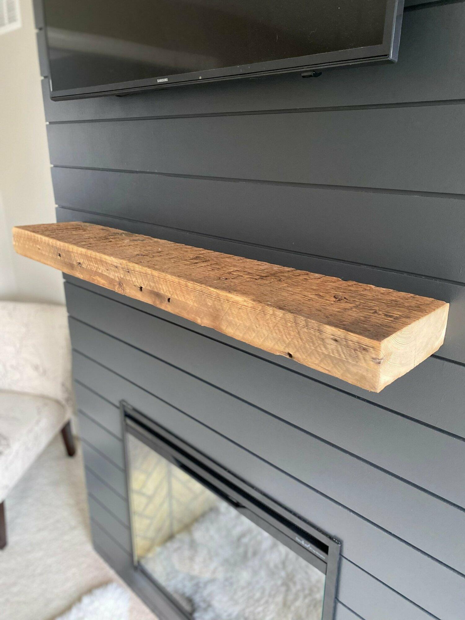 a reclaimed barnwood floating fireplace mantel. Shown natural on a shiplap fireplace with nail holes and saw marks displayed.