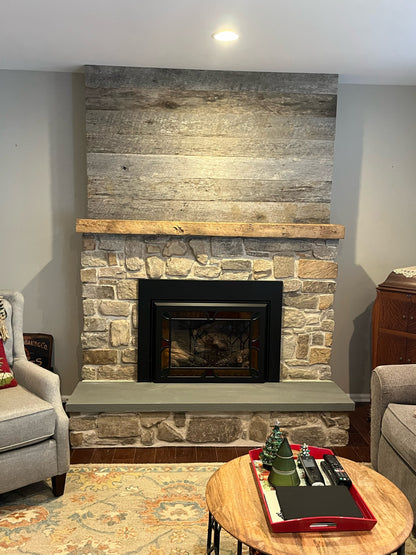 weathered grey barnwood paneling on a fireplace surround with a mantel displayed. Grey barnwood paneling shows wood texture and contrasts yet compliments the natural mantel mounted.