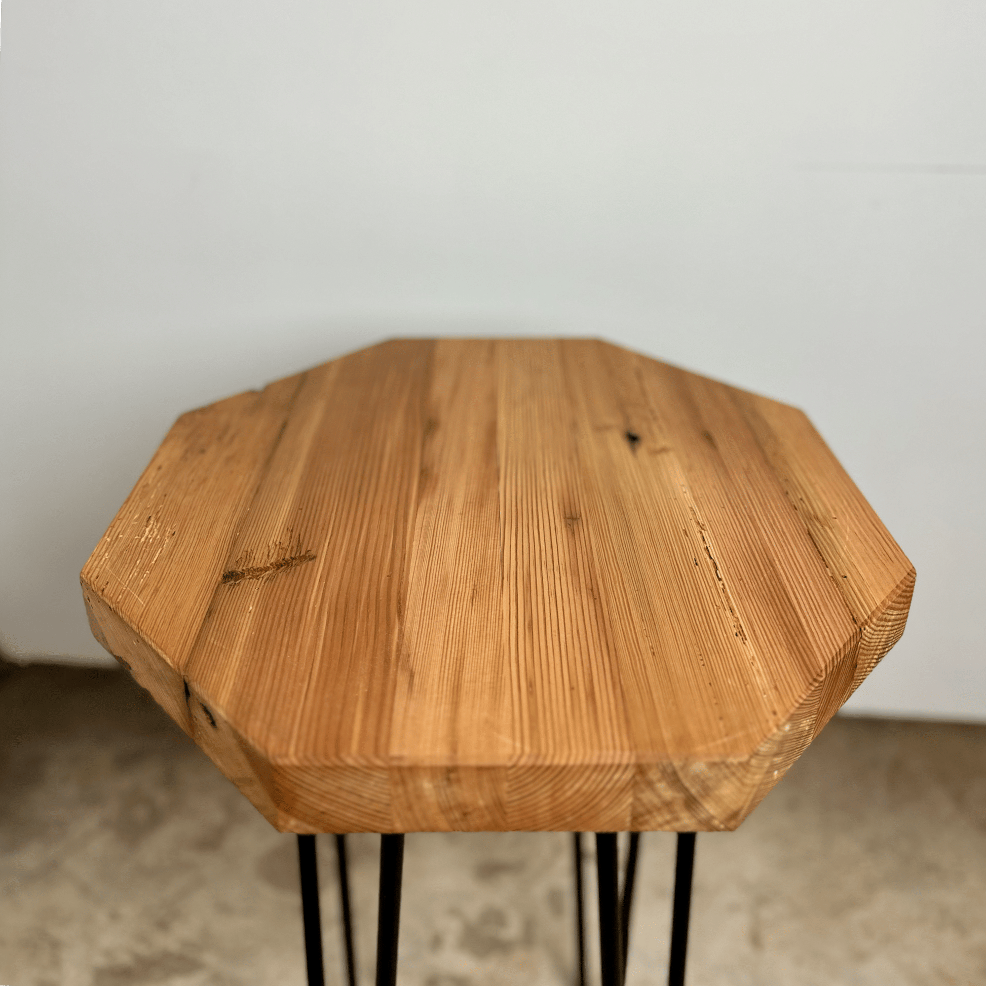 a reclaimed wood table in an octagonal shape and oil finish. The table is supported by four hairpin legs. Grain patterns and color variations in the wood are shown.
