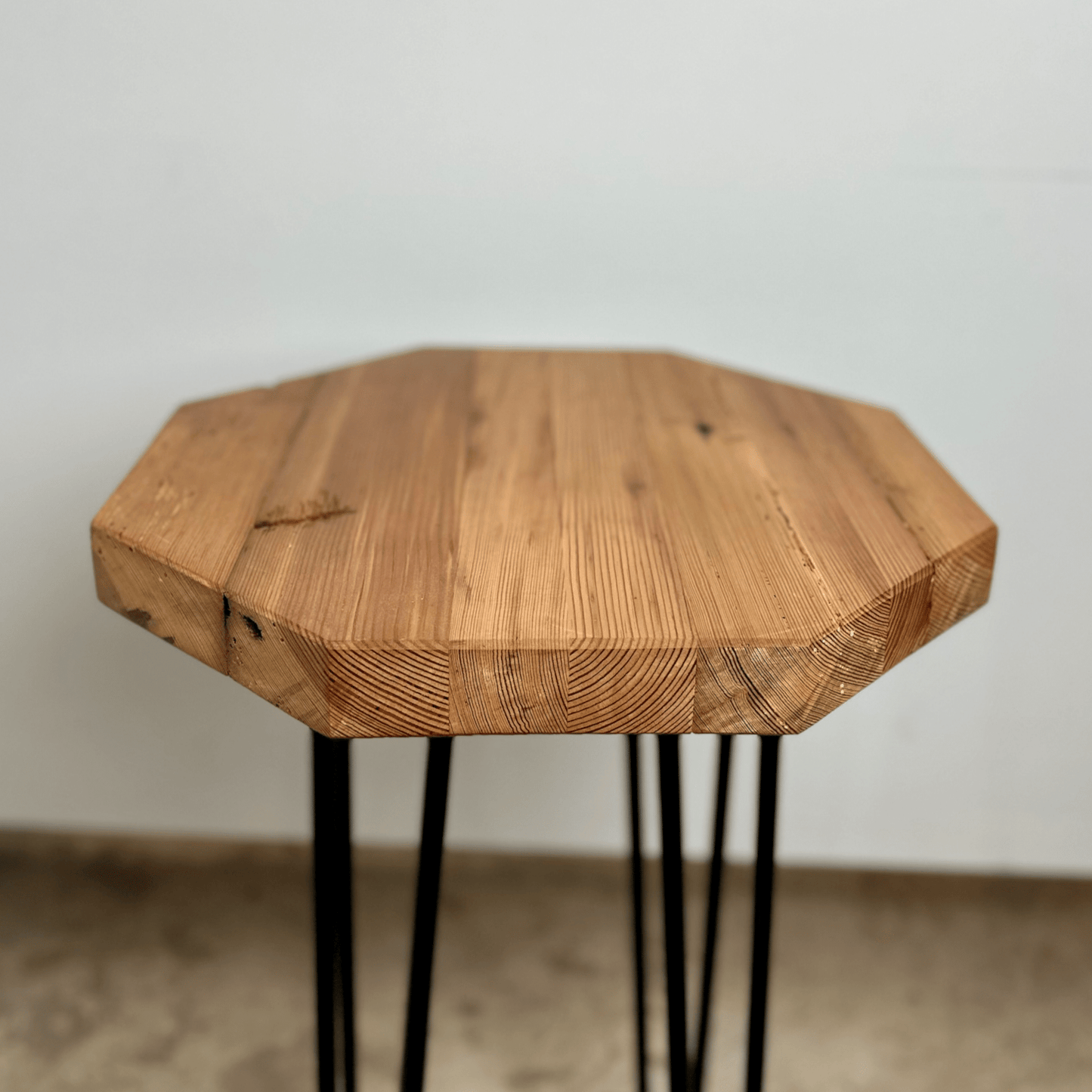 a reclaimed wood table in an octagonal shape and oil finish. The table is supported by four hairpin legs. Grain patterns and color variations in the wood are shown.