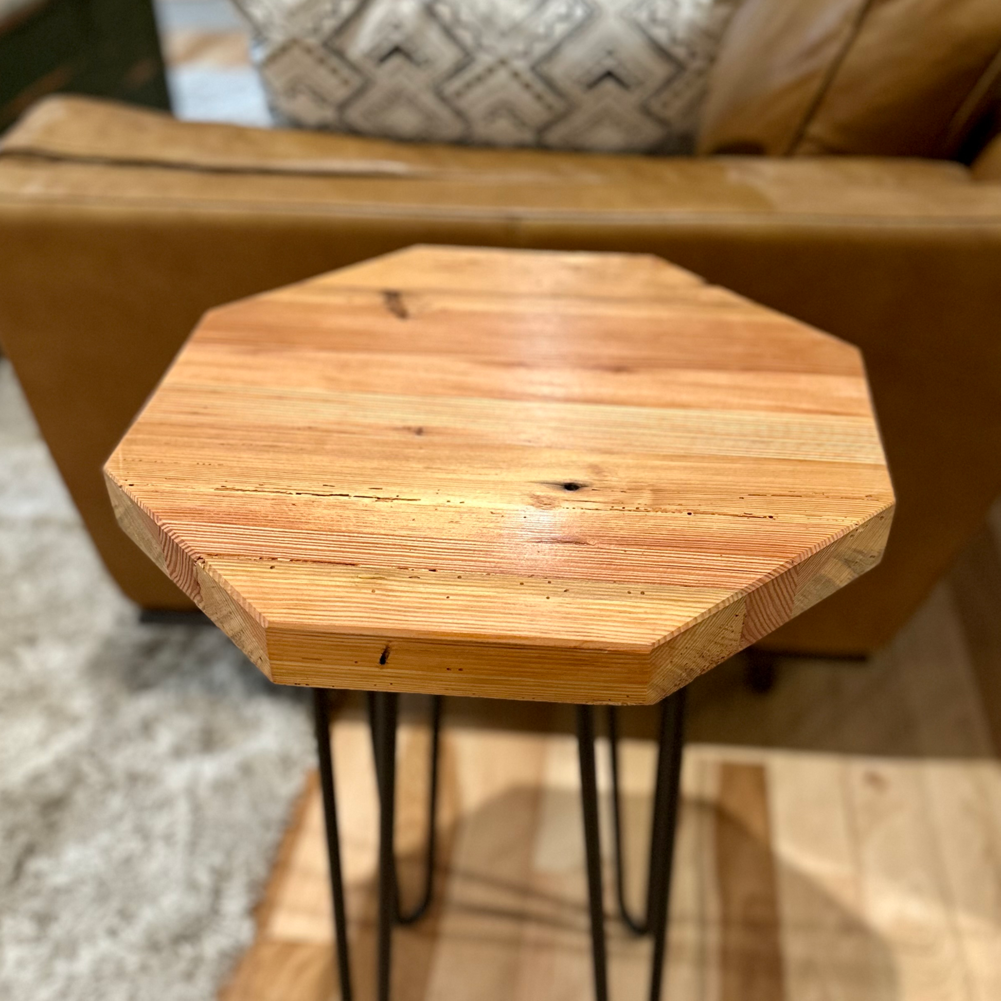 a reclaimed wood table in an octagonal shape and lacquer finish. The table is supported by four hairpin legs and is shown next to a couch as a side table.