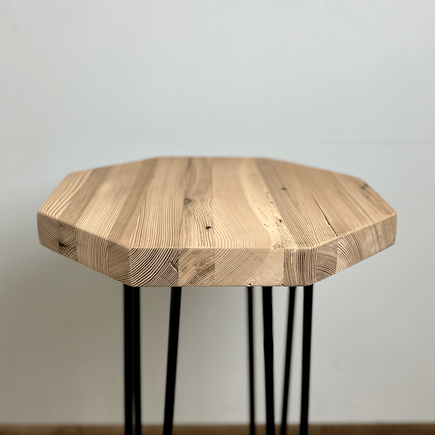 a reclaimed wood table in an octagonal shape and unfinished finish. The table is supported by four hairpin legs. Grain patterns and color variations in the wood are shown.