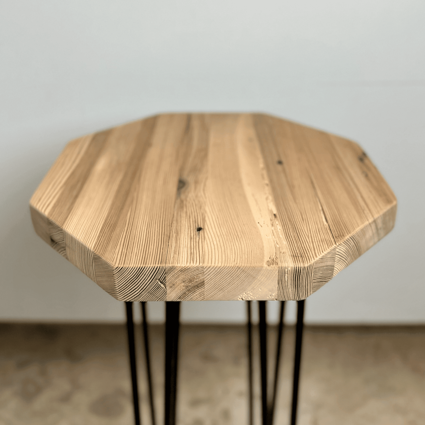 a reclaimed wood table in an octagonal shape and unfinished finish. The table is supported by four hairpin legs. Grain patterns and color variations in the wood are shown.