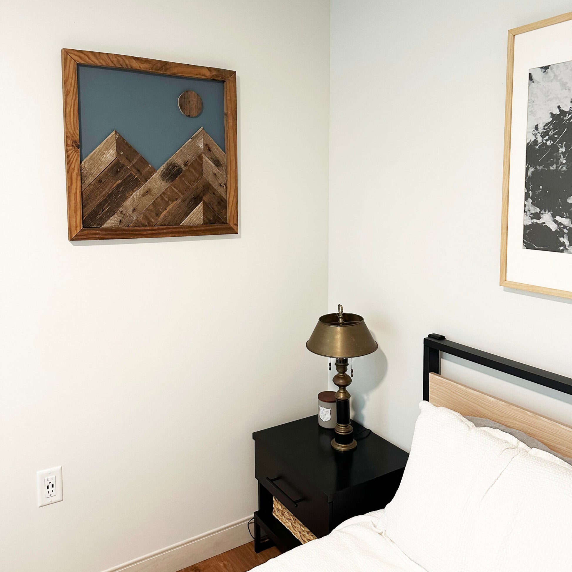wall decor that looks like two mountains with a full moon overtop. Mountains, moon, and frame of wall decor all made from reclaimed barnwood. Wood shows grain patterns and other distressed characteristics. Mounted on a wall in a bedroom setting.