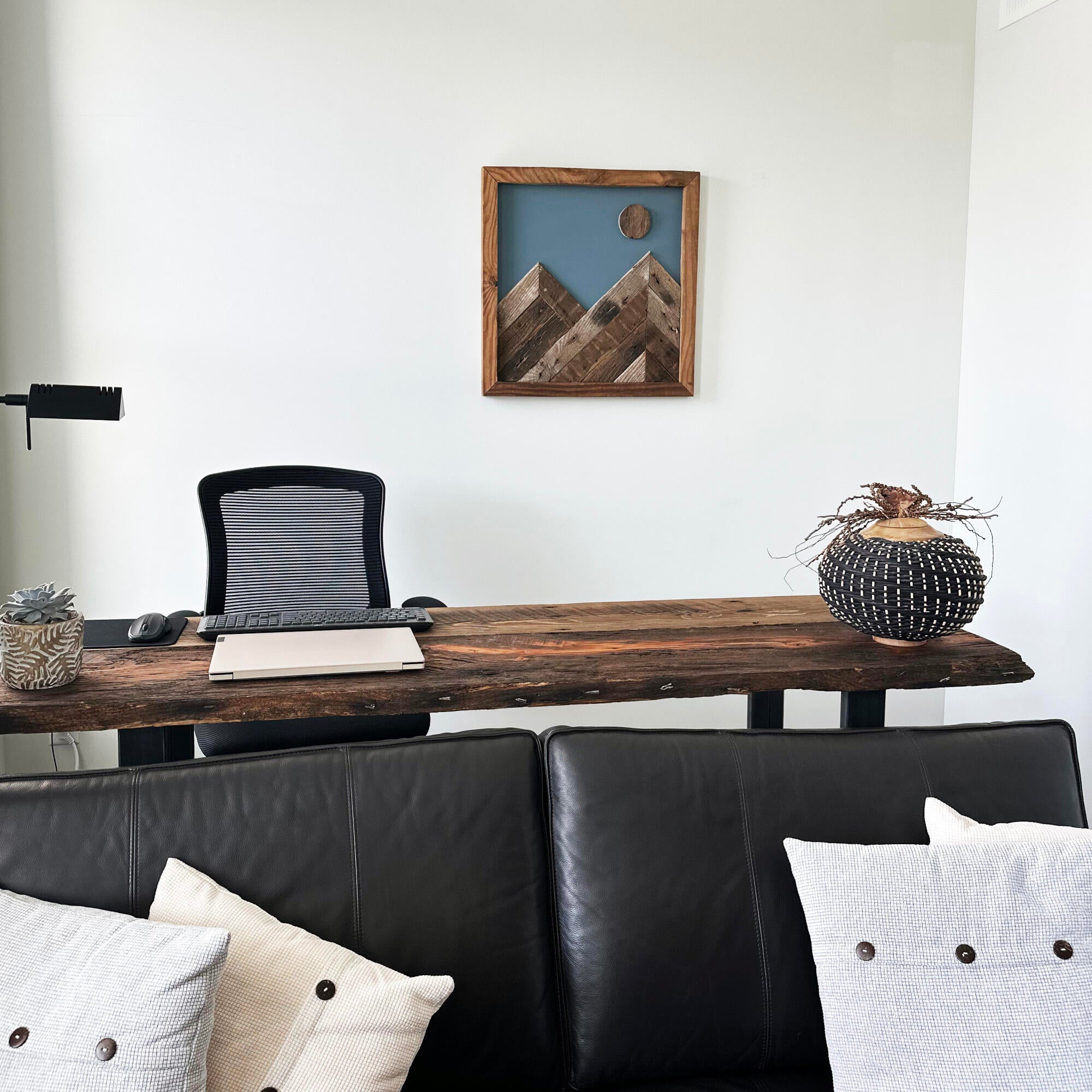 wall decor that looks like two mountains with a full moon overtop. Mountains, moon, and frame of wall decor all made from reclaimed barnwood. Wood shows grain patterns and other distressed characteristics. Mounted on a wall in an office setting.