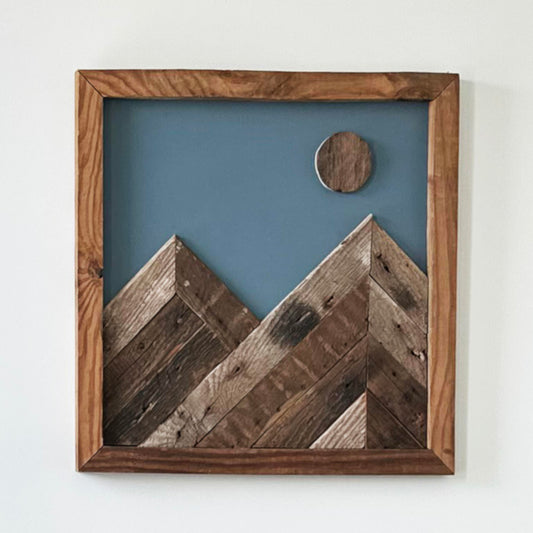 wall decor that looks like two mountains with a moon overtop. Mountains, moon, and frame of wall decor all made from reclaimed barnwood. Wood shows grain patterns and other distressed characteristics.