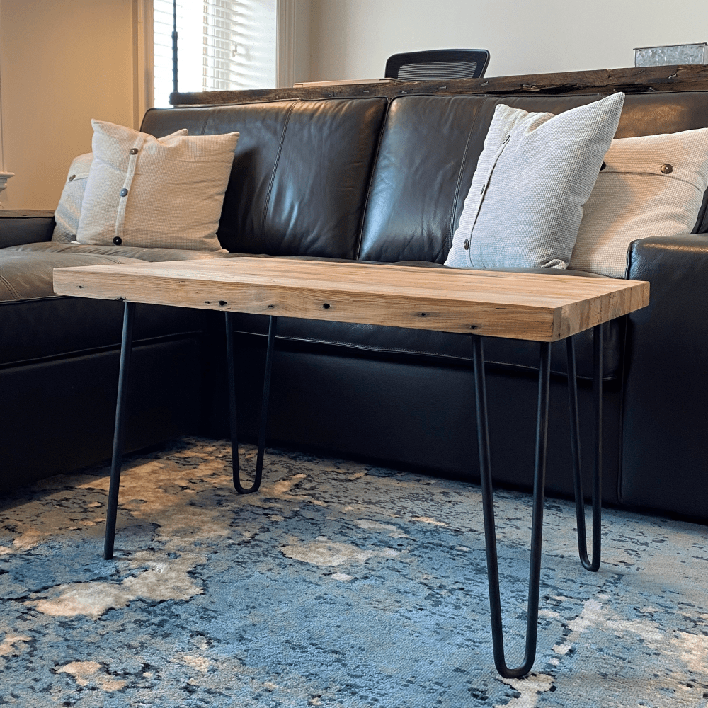 A reclaimed wood coffee table with hair pin legs from a side view and in a  living room setting. The view shows nail holes and the grain pattern in the wood.