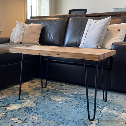 A reclaimed wood coffee table with hair pin legs from a side view and in a  living room setting. The view shows nail holes and the grain pattern in the wood.