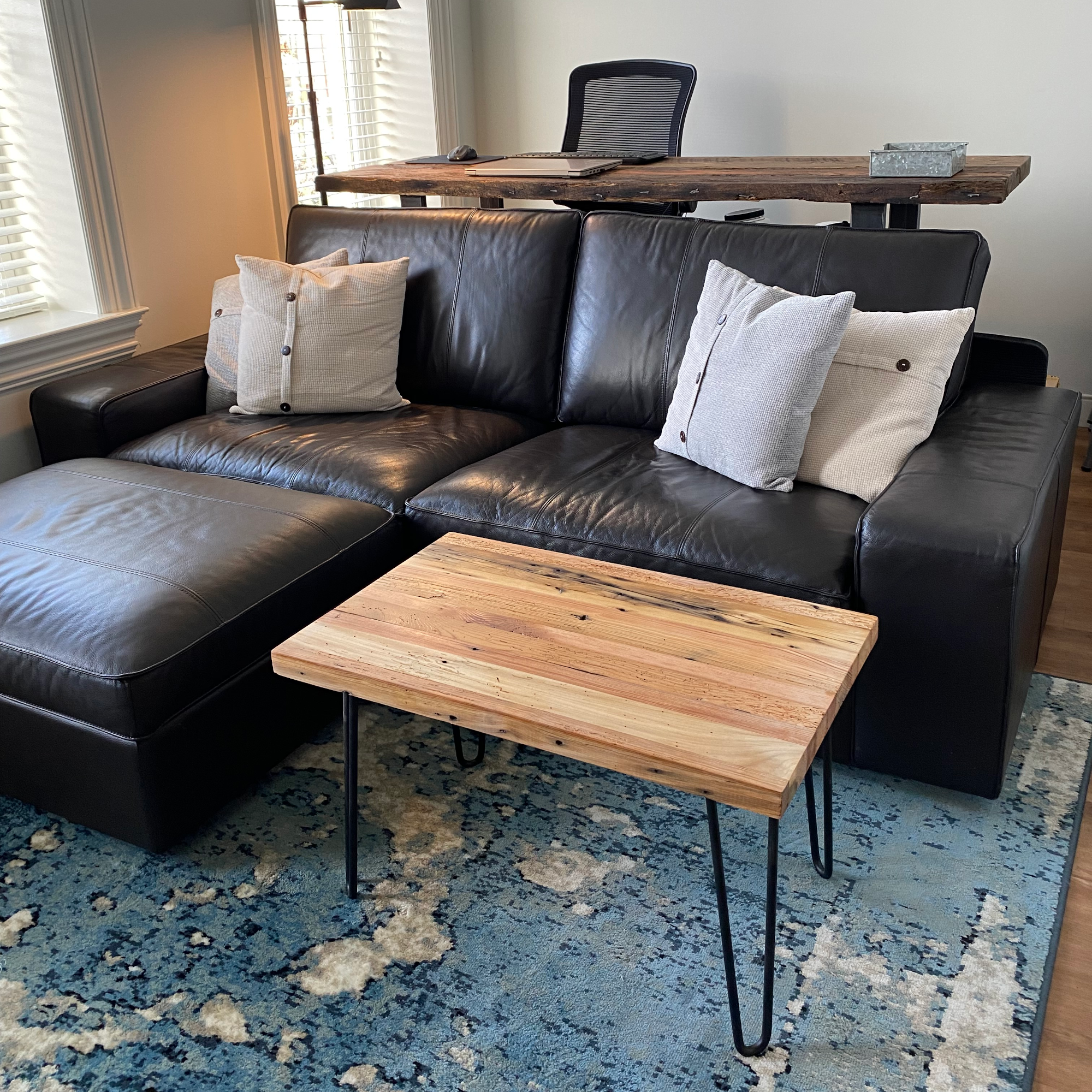 A reclaimed wood coffee table with hair pin legs in a wider view and living room setting. The view shows variations in the wood and rustic characteristics. The lacquer finish shown adds a slight shine.