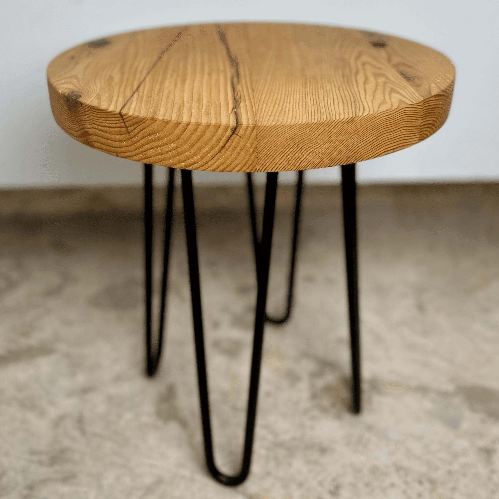 a reclaimed wood table in an round shape and sealed unfinished finish. The table is supported by four hairpin legs. Checking and grain patterns present in the wood.