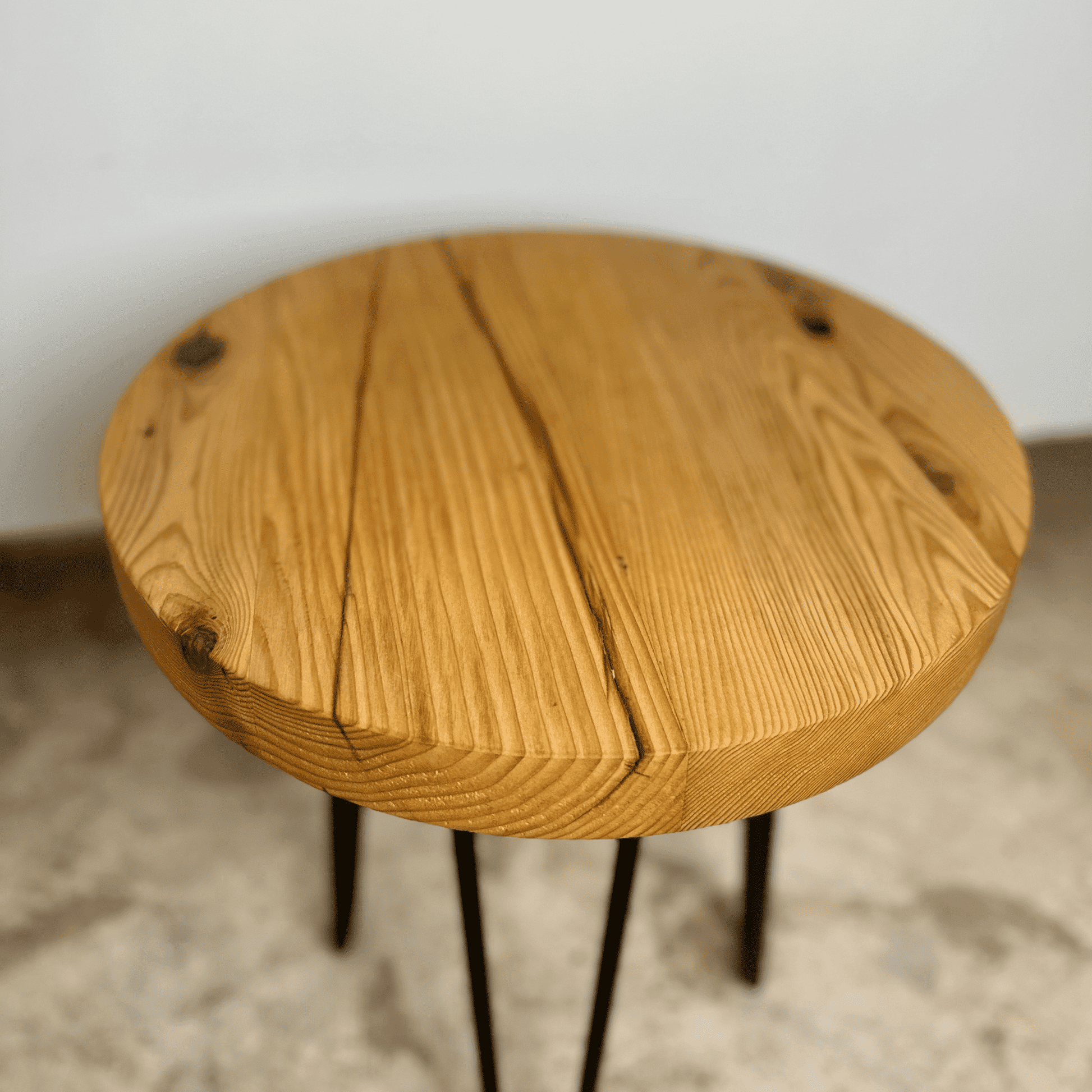 a reclaimed wood table in an round shape and sealed unfinished finish. The table is supported by four hairpin legs. Checking and grain patterns present in the wood.