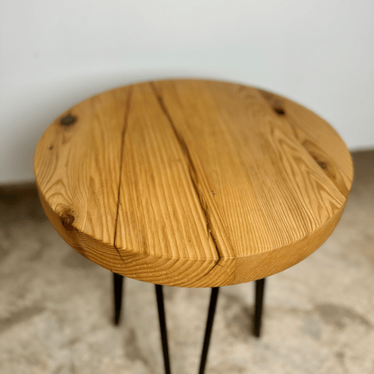 a reclaimed wood table in an round shape and sealed unfinished finish. The table is supported by four hairpin legs. Checking and grain patterns present in the wood.