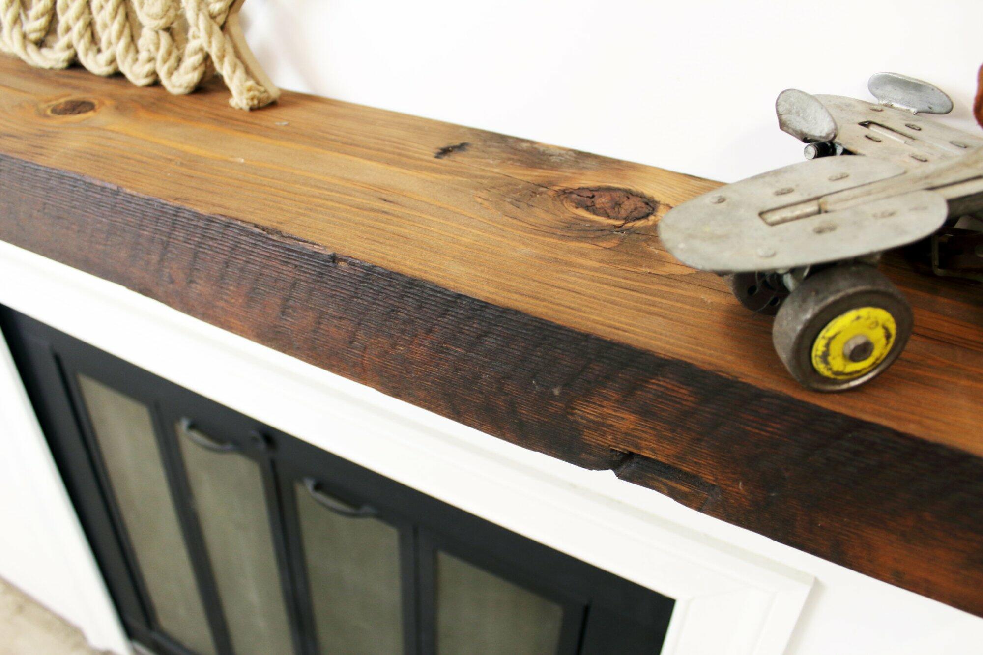 close up of skip-planed reclaimed barnwood fireplace mantel. Front face is darker than top side of mantel and prominent grain patterns and knots are shown.