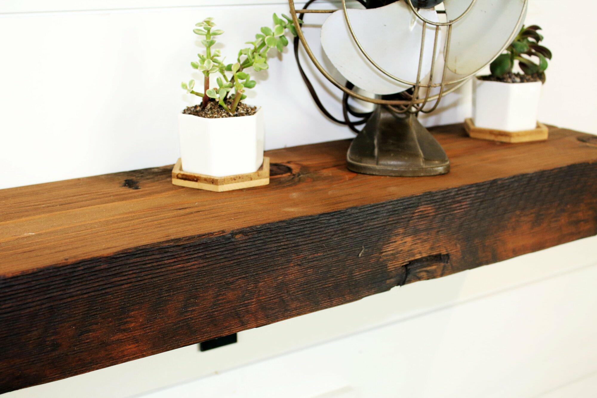 close up of skip-planed reclaimed barnwood fireplace mantel. Front face is darker than top side of mantel and prominent grain patterns and knots are shown.