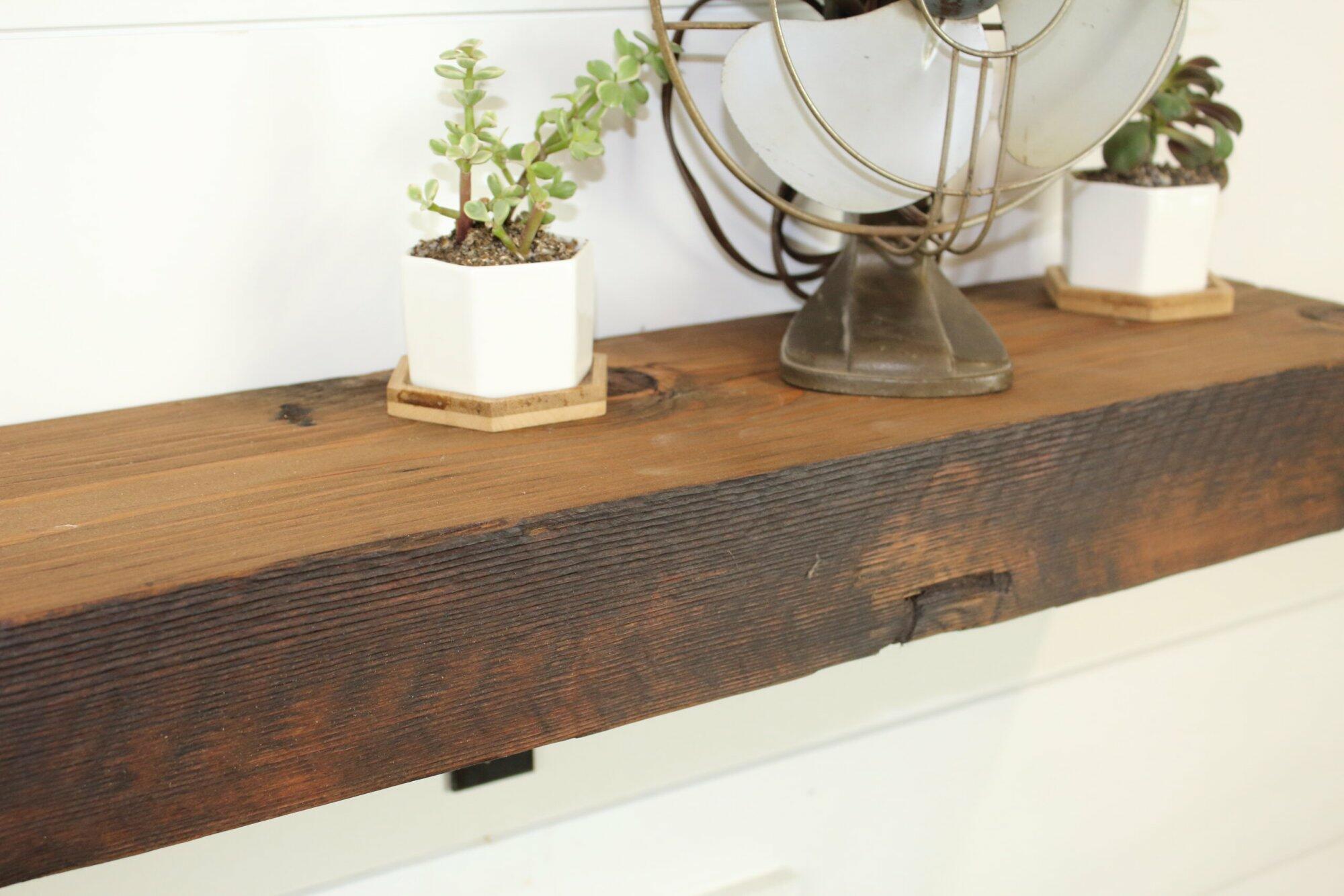 close up of skip-planed reclaimed barnwood fireplace mantel. Front face is darker than top side of mantel and prominent grain patterns and knots are shown.