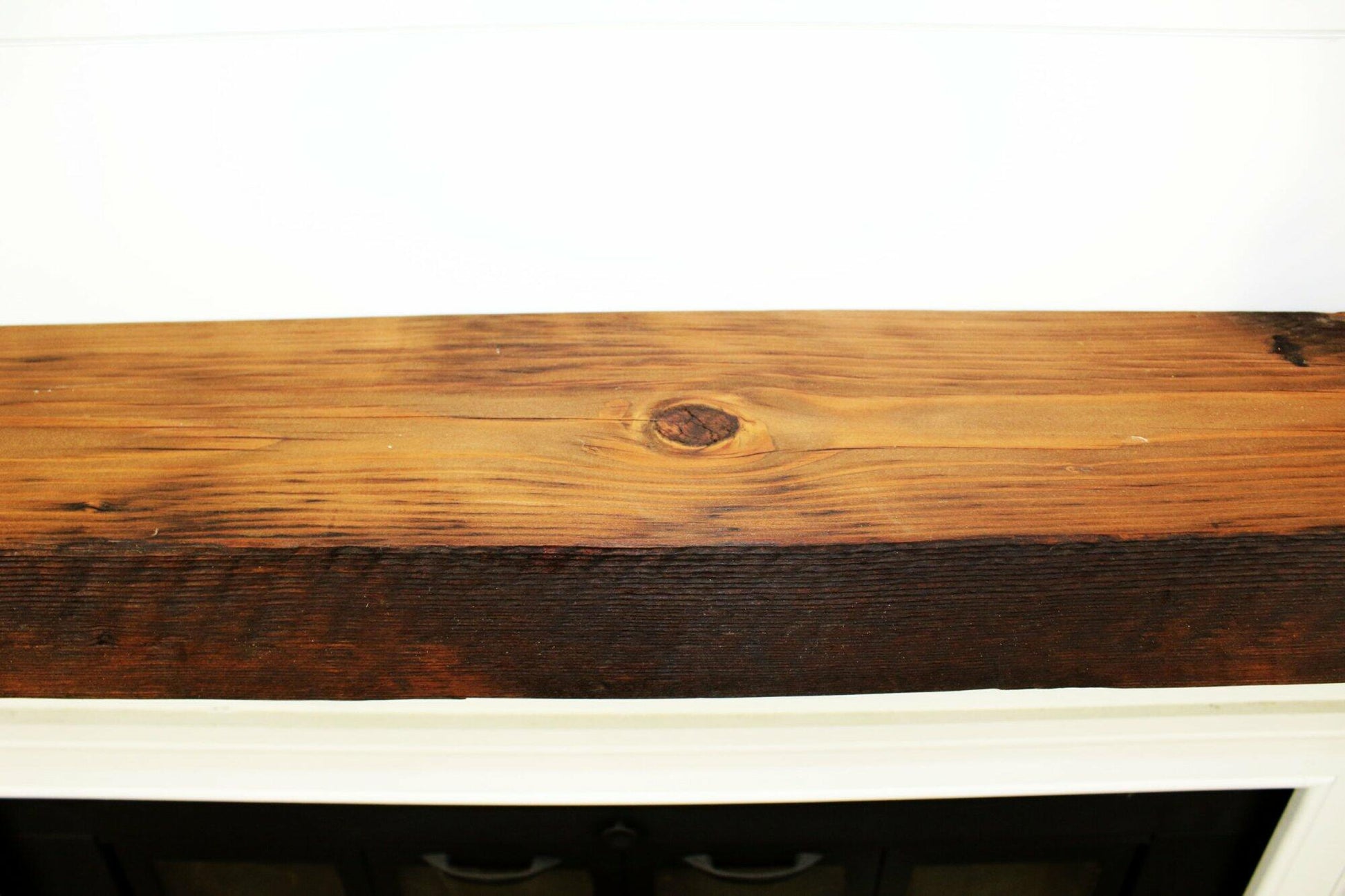 close up of skip-planed reclaimed barnwood fireplace mantel. Front face is darker than top side of mantel and prominent grain patterns and knots are shown.