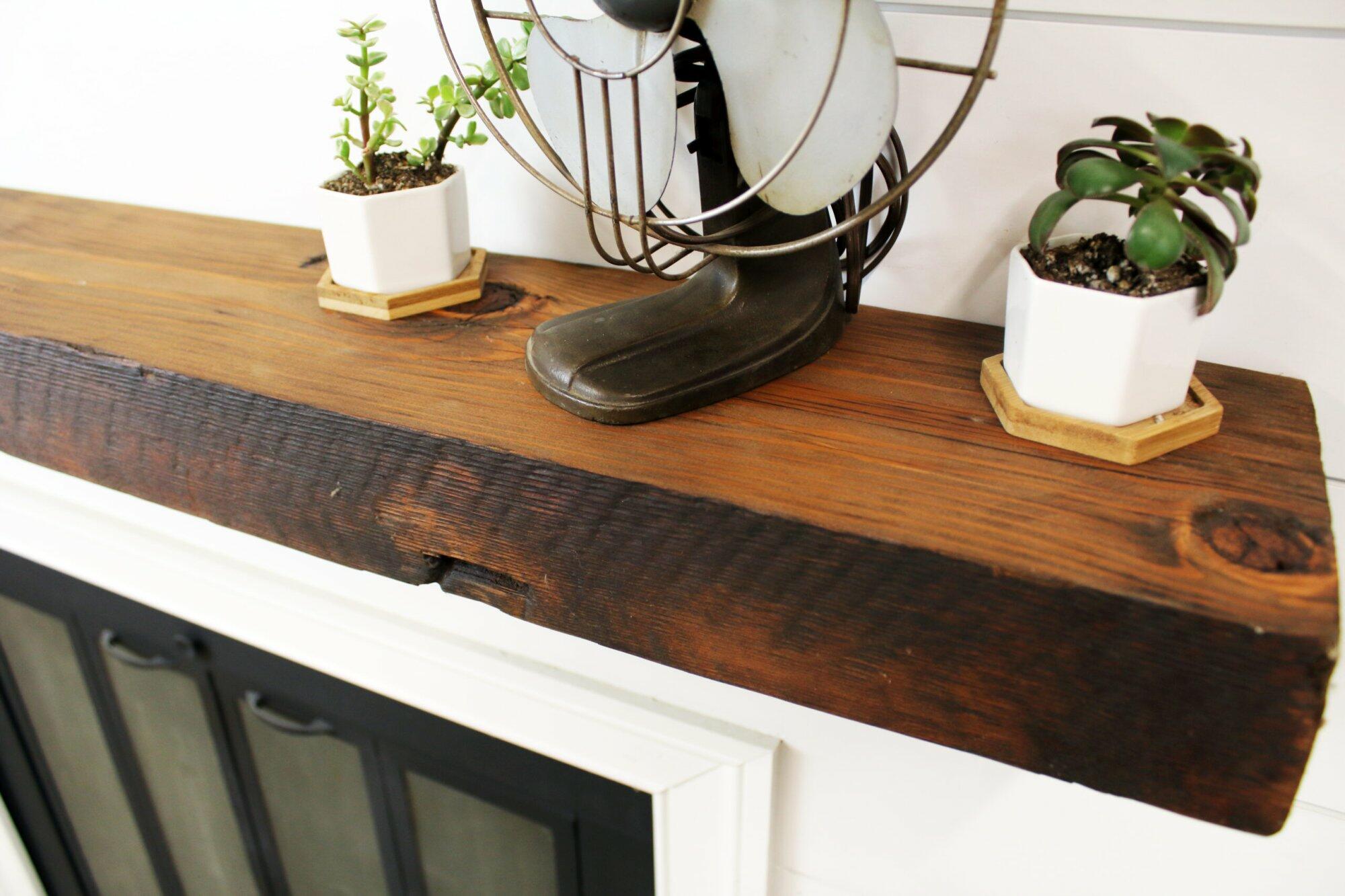 close up of skip-planed reclaimed barnwood fireplace mantel. Front face is darker than top side of mantel and prominent grain patterns and knots are shown.