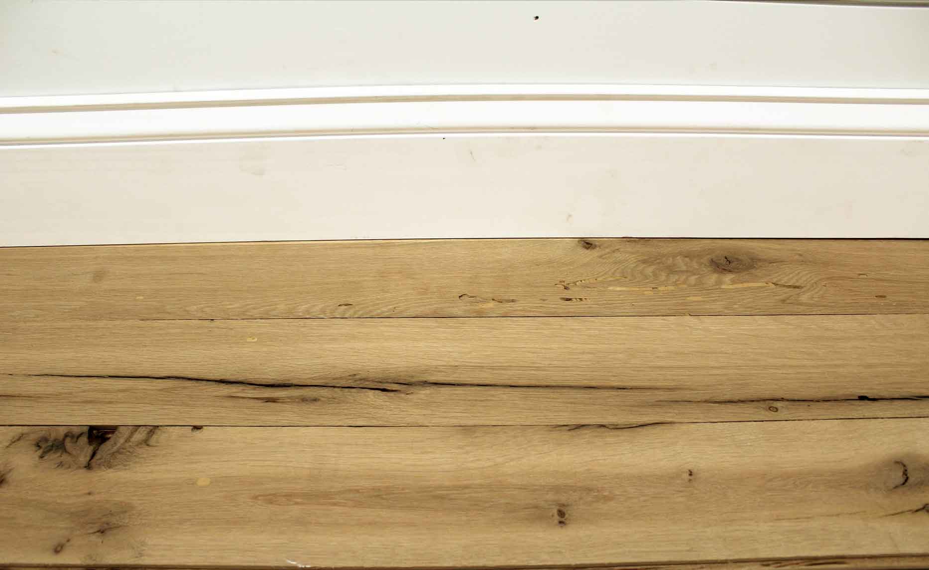 reclaimed white oak flooring installed with baseboard molding. Variations in wood color shown along with knots, checking, and characteristics from previous bug activity.