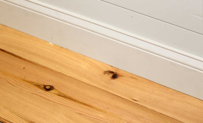yellow pine reclaimed wood flooring installed with baseboard. Flooring shows knots and prominent grain patterns.