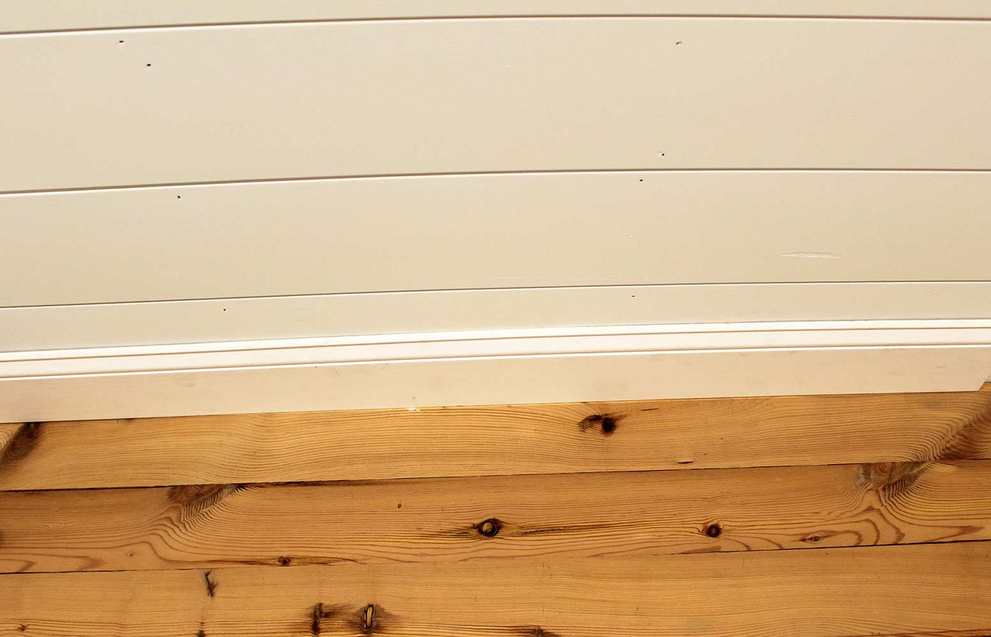 yellow pine reclaimed wood flooring installed with baseboard. Flooring shows knots and prominent grain patterns.